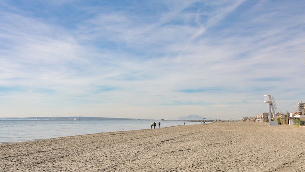 A beach with a lifeguard tower, a sandy shore, and buildings in the background.