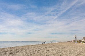 Ein Strand mit einem Rettungsturm, sandigem Ufer und Gebäuden im Hintergrund.