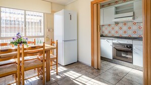 A kitchen with a refrigerator, oven, and dining area with chairs and a table.