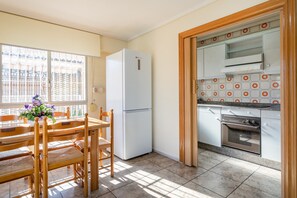 A kitchen with a refrigerator, oven, and dining area with chairs and a table.