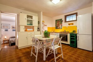 A compact kitchen with white cabinets, a dining table with chairs, a refrigerator, and a window with a view.