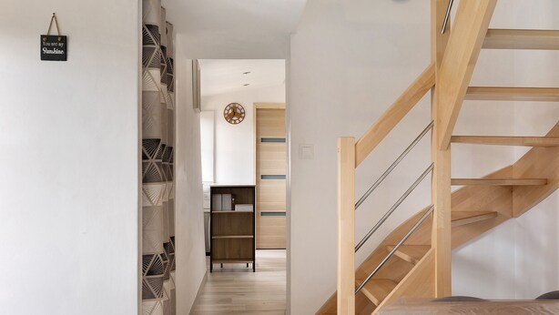 Ein modernes Interieur mit einer Holztreppe, einem zur Küche führenden Flur und einer dekorativen Wanduhr.