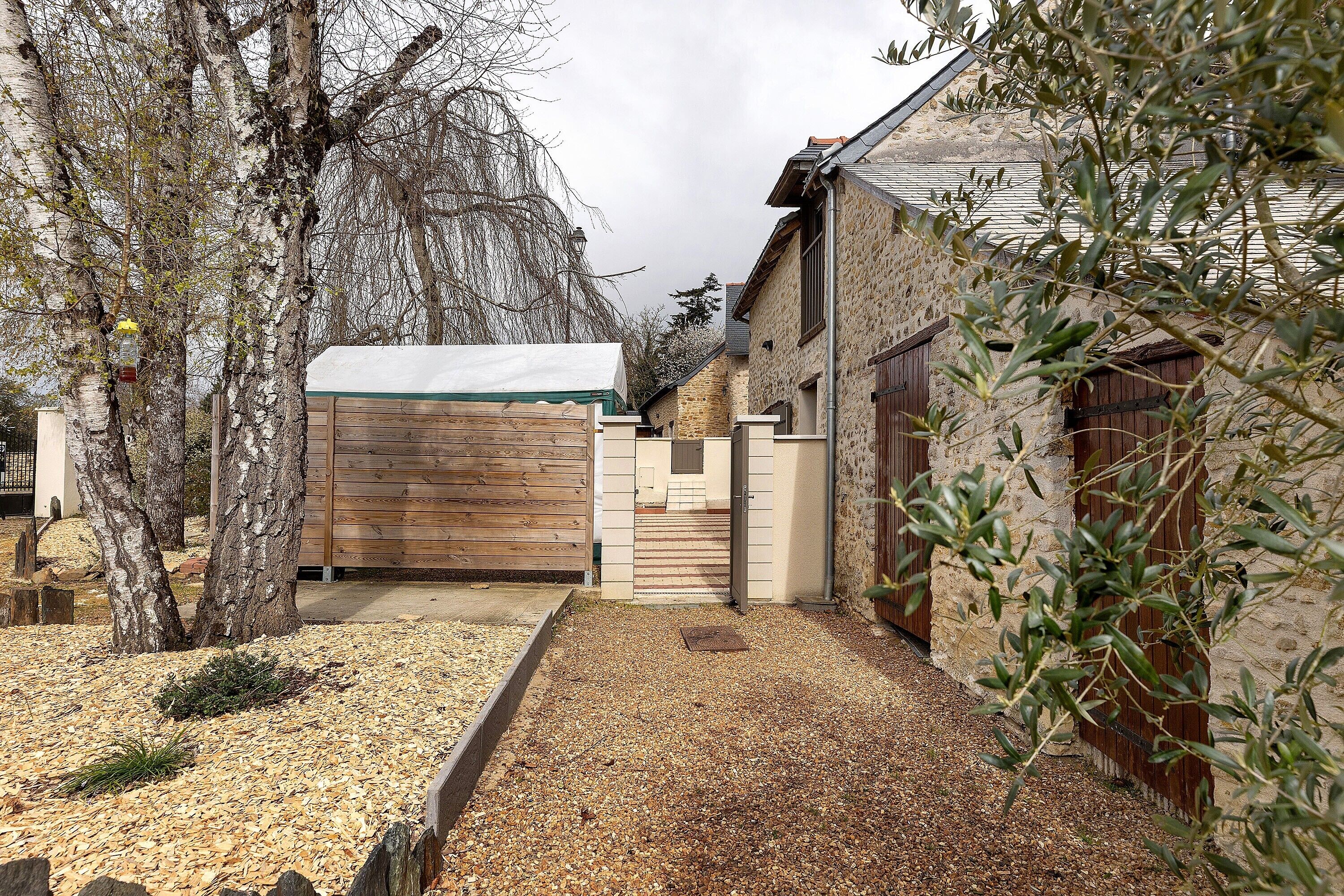 A courtyard with a wooden gate, stone walls, and a gravel path.