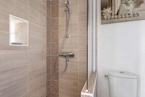 Un baño moderno con ducha, inodoro y una figura de ángel decorativa en la pared.