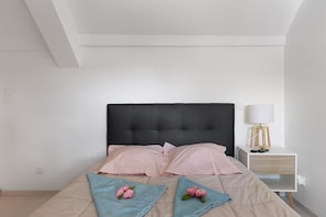 A neatly made bed with a black headboard, two pink pillows, and a beige blanket.