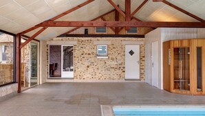 An indoor swimming pool area with stone walls, wooden beams, and a glass door leading to a patio.