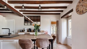 A kitchen with a wooden island, pendant lights, a clock, and a vase with flowers.