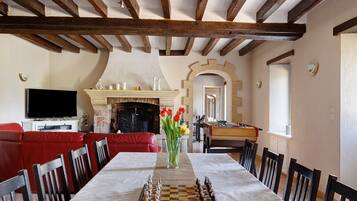 A dining area with a chessboard, a fireplace, and a television in a room with exposed wooden beams and a red sofa.