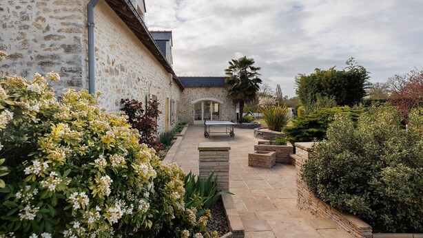 A stone building with a paved patio, a table, and various plants.