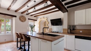 A kitchen with a wooden island, white cabinets, a clock, and a window with a view of greenery.