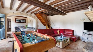 A living room with a foosball table, red sofa, and a staircase.
