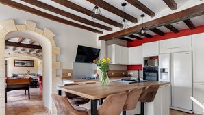 Uma cozinha moderna com uma ilha de madeira, banquetas e uma TV fixada na parede.