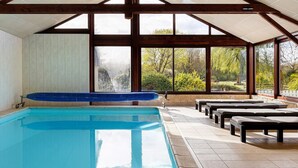 Piscina com banheira de hidromassagem, bancos e amplas janelas com vista para árvores e uma cachoeira.