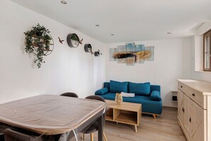 Un salon moderne comprenant une table à manger, un canapé bleu, une table basse en bois et un arrangement de plantes fixé au mur.