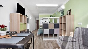 Een moderne woonkamer met een bank, een eettafel met stoelen, een televisie op een standaard en een boekenkast.