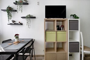 Moderni olohuone, jossa on televisio, hyllykkö ja amppelikasveja.