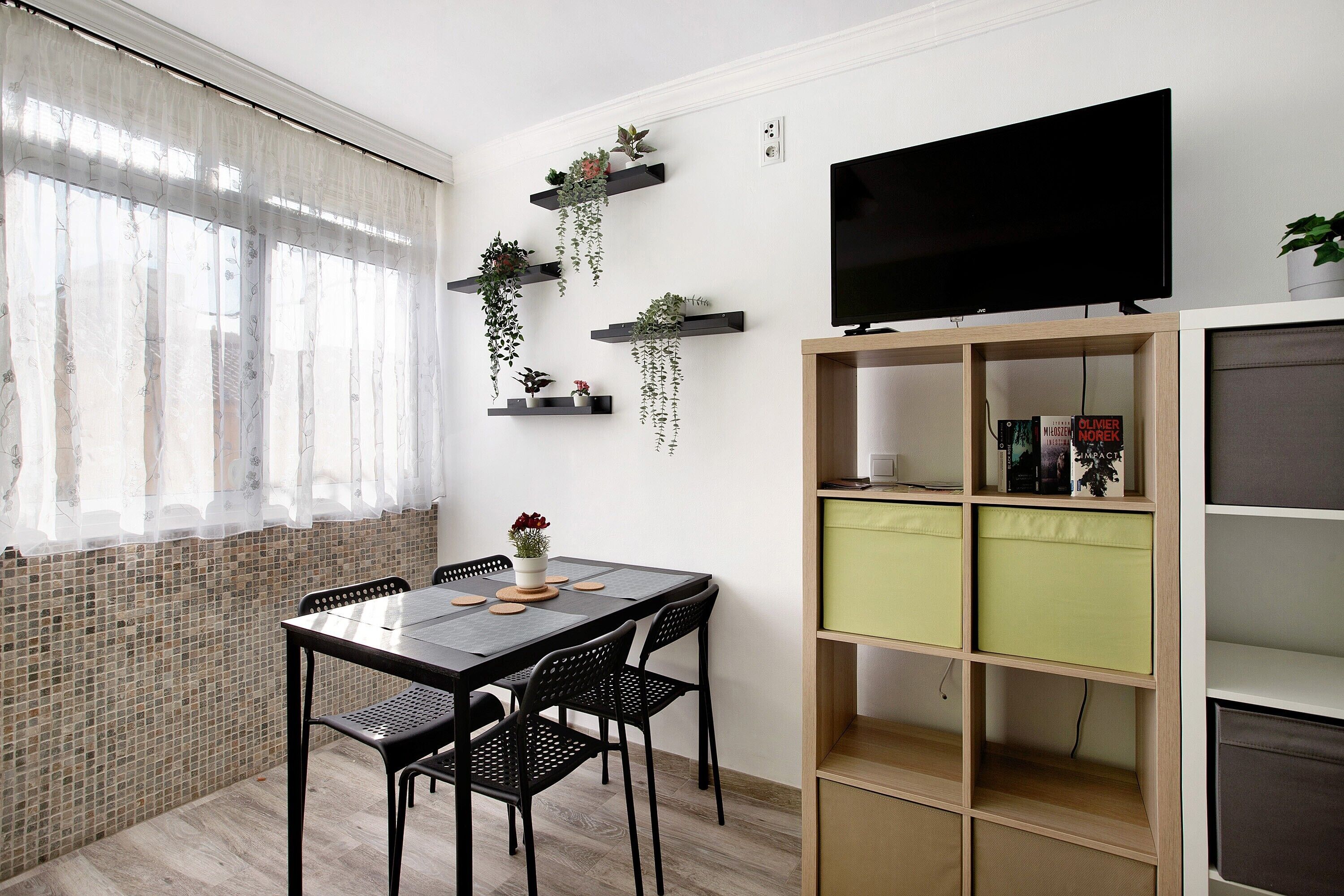 Quarto com mesa de jantar, cadeiras, televisão e prateleiras com plantas.