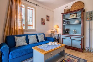 Un divano blu con cuscini decorati, un tavolino in legno con un vassoio di teiere bianche e un armadio con bicchieri e stoviglie.
