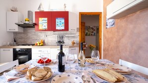 Una mesa de comedor dispuesta con platos, pan, vino y vasos en una cocina con un armario rojo y salpicadero de azulejos.
