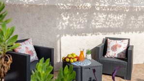 Dos sillones de mimbre con cojines estampados, una mesita con fruta, un vaso de zumo de naranja y una planta en maceta.