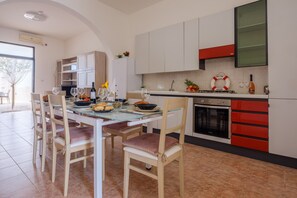 A modern kitchen with white cabinets, a red accent wall, and a dining area with a glass table and chairs. - Villa 'Maestrale Torre Lapillo' with Private Terrace, Wi-Fi and Air Conditioning (Porto Cesareo)