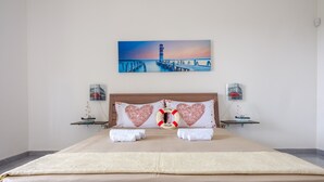 A hotel room with a bed, heart-shaped pillows, a life preserver decoration, a painting of a lighthouse, and two small tables with decorative items. - Villa 'Perla Marina Luxury' with Sea View, Wi-Fi and Air Conditioning (TOTTE LAPILLO)