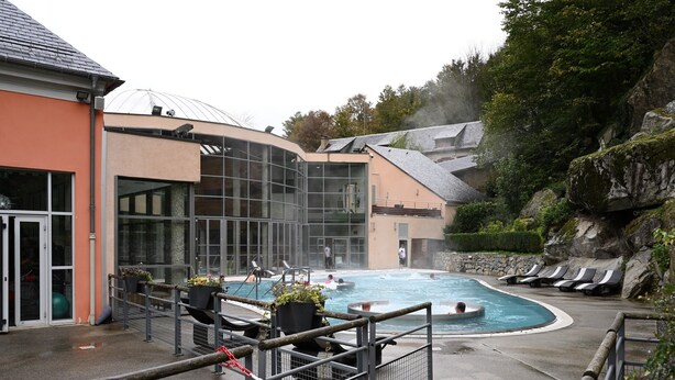 A swimming pool area with a glass-enclosed building, lounge chairs, and a rocky hillside backdrop. - Central Cauterets, Private Parking, Walk to Thermal Baths & Ski Lifts (Cauterets)