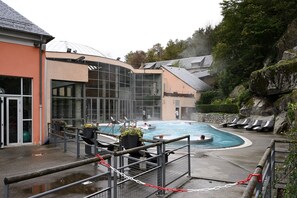 A swimming pool area with a glass-enclosed building, lounge chairs, and a rocky hillside backdrop.