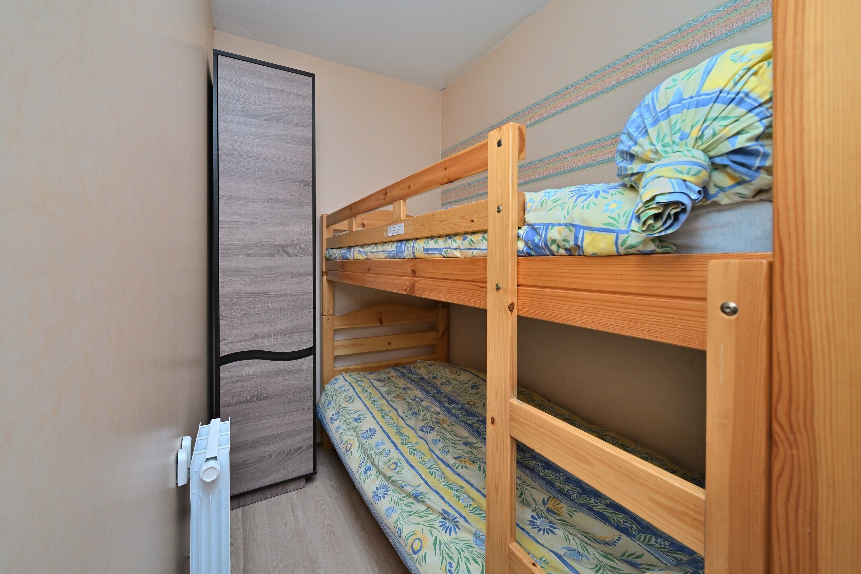 Una cama litera con una colcha estampada, un armario de madera y un radiador.