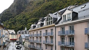 A row of multi-story buildings with balconies, set against a mountainous backdrop. - Central Cauterets, Private Parking, Walk to Thermal Baths & Ski Lifts (Cauterets)
