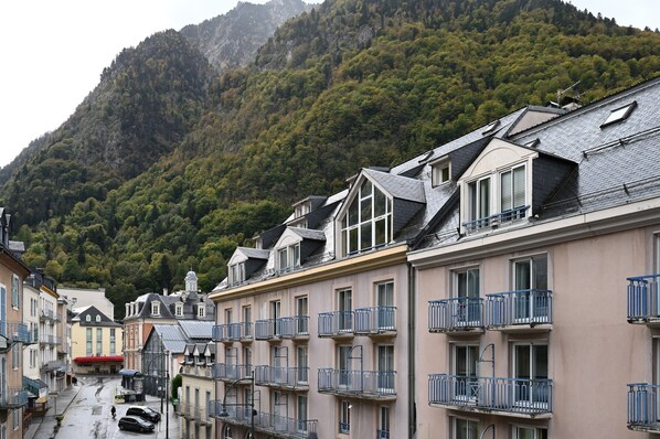 A row of multi-story buildings with balconies, set against a mountainous backdrop.