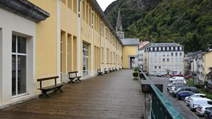 A wooden deck with benches, a row of yellow buildings, and a church spire in the background. - Central Cauterets, Private Parking, Walk to Thermal Baths & Ski Lifts (Cauterets)