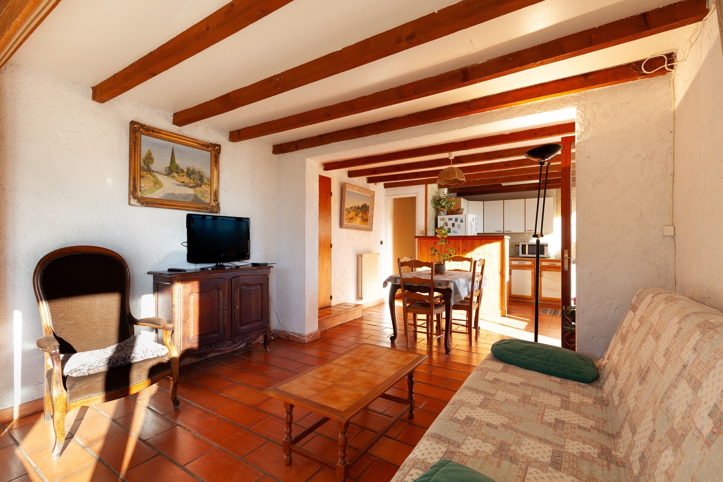 A living room with a sofa, a wooden table, a TV on a cabinet, and a painting on the wall.