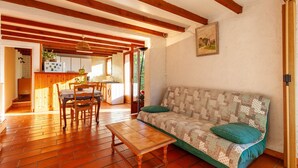 A cozy living room with a wooden floor, a sofa with a quilt, a wooden coffee table, and a dining area with chairs and a table. - Studio Apartment 'Ukika' with Sea View, Wi-Fi and Air Conditioning (cassis)