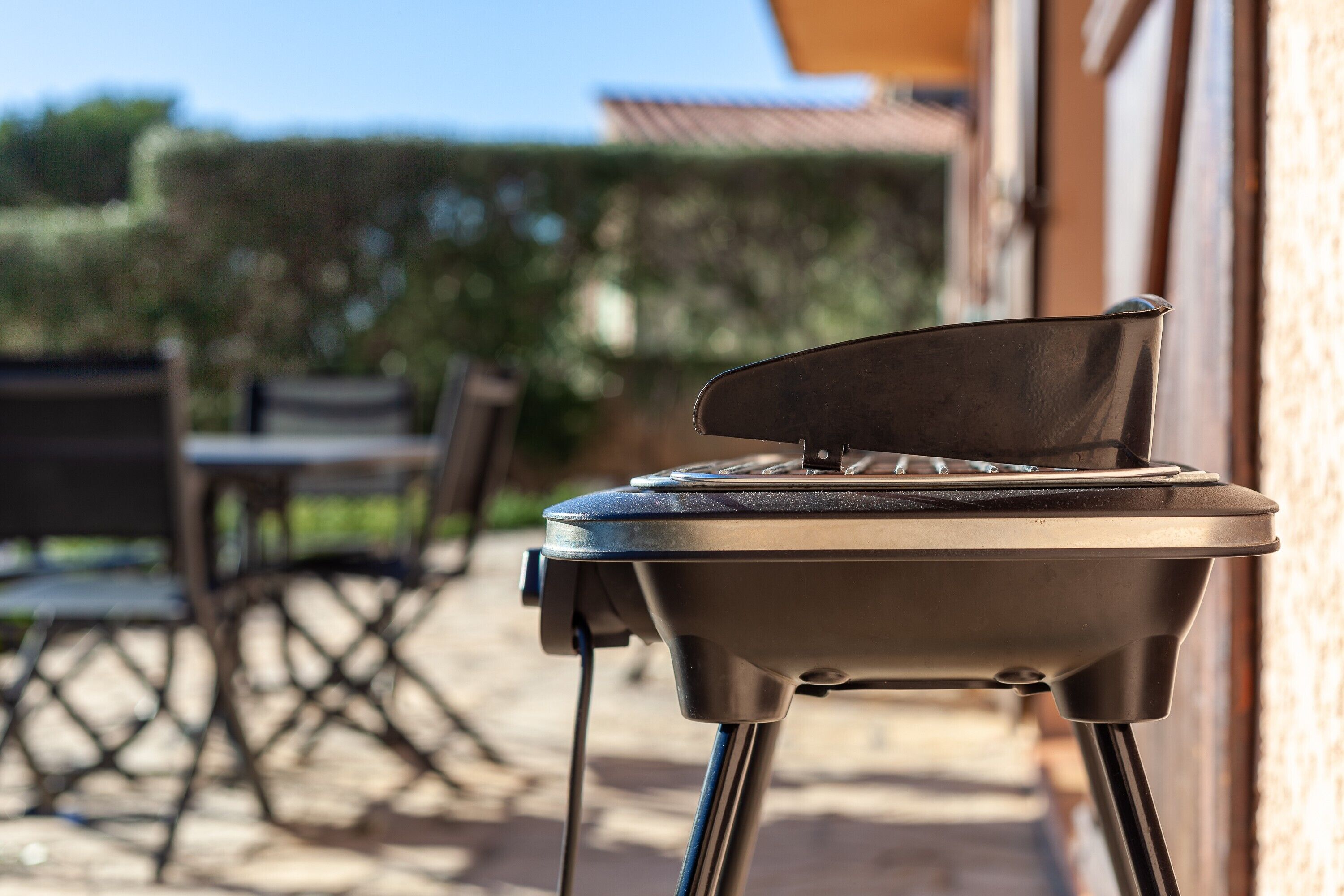A barbecue grill outdoors with a patio table and chairs in the background.