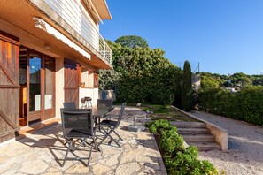 A stone patio with outdoor furniture, a wooden door, and a view of a lush garden and trees.