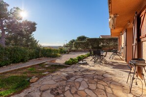 Un patio in pietra con mobili da esterno, un barbecue e vista sul mare.