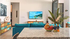 A modern living room with a teal sofa, a marble coffee table, and a painting of a coastal landscape.