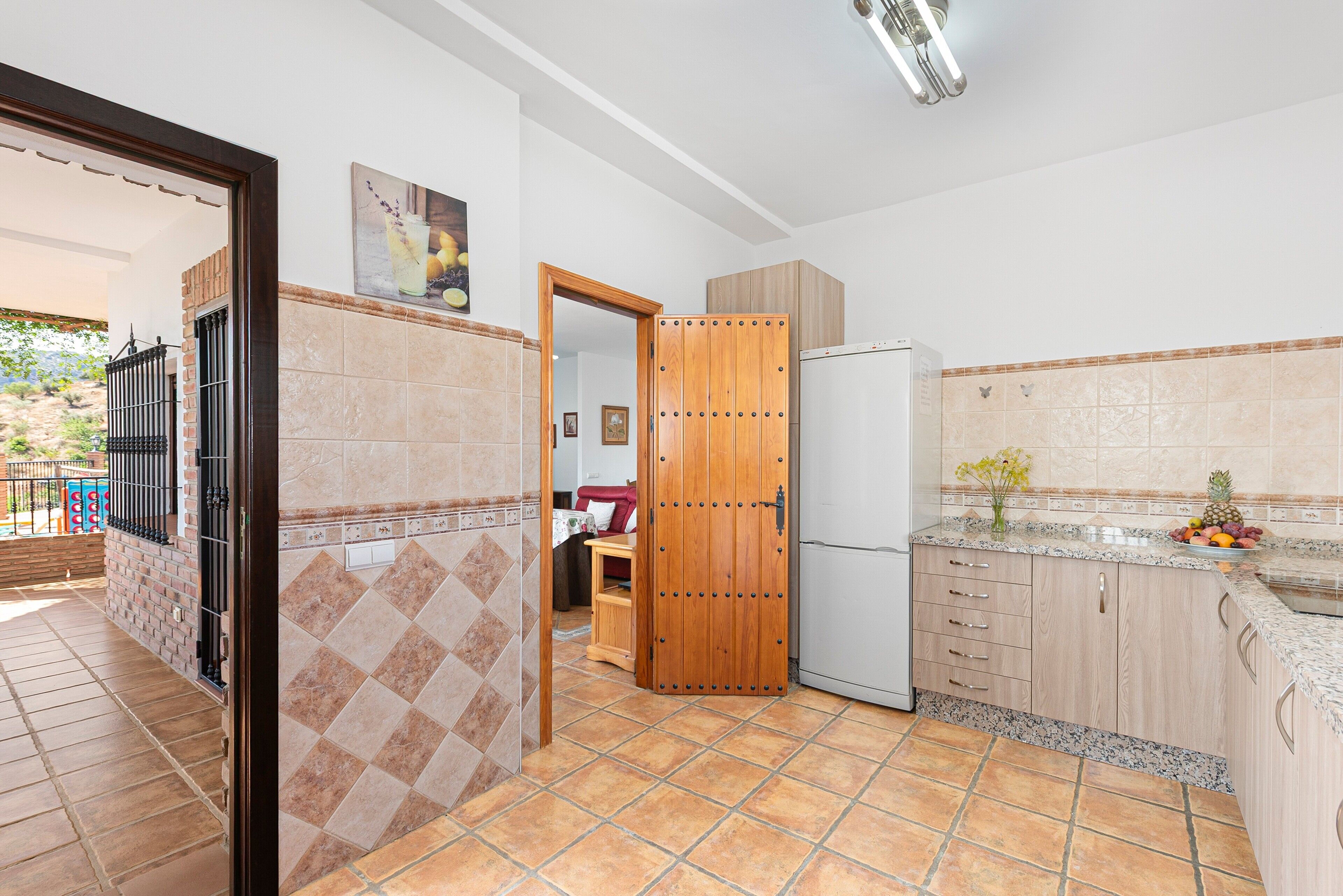 Eine Küche mit Kühlschrank, Holzschränken, einer gefliesten Spritzschutzwand und einer Tür zu einem anderen Raum.