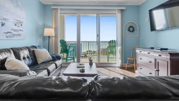 A living room with a leather couch, a coffee table, a TV, and a balcony with green chairs. - Breathtaking 16th-Floor Gulf Views • Sleeps 8 • Ariel Dunes II (Destin)