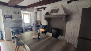 A kitchen with a stone wall, wooden beams, a dining table, chairs, a stove, and a window.