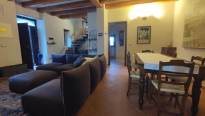 A living room with a sofa, a dining table with chairs, a staircase, and a kitchen area. - Holiday Home 'Gnazzano Home' with Mountain View, Wi-Fi and Air Conditioning (Loiano)