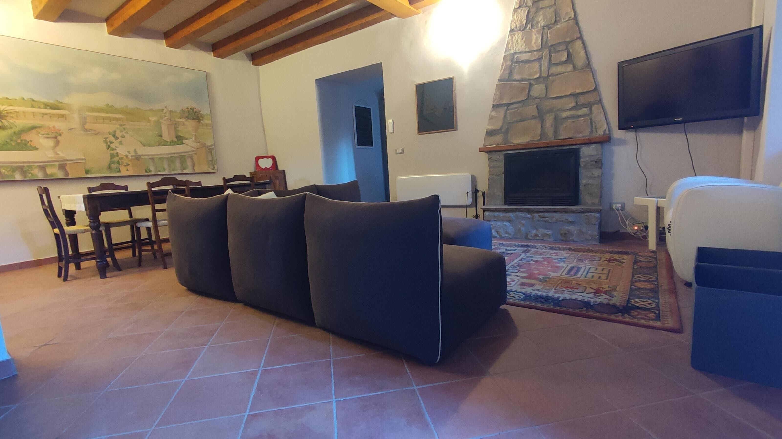 Uma sala de estar com lareira de pedra, televisão na parede e área de refeições com cadeiras e mesa.