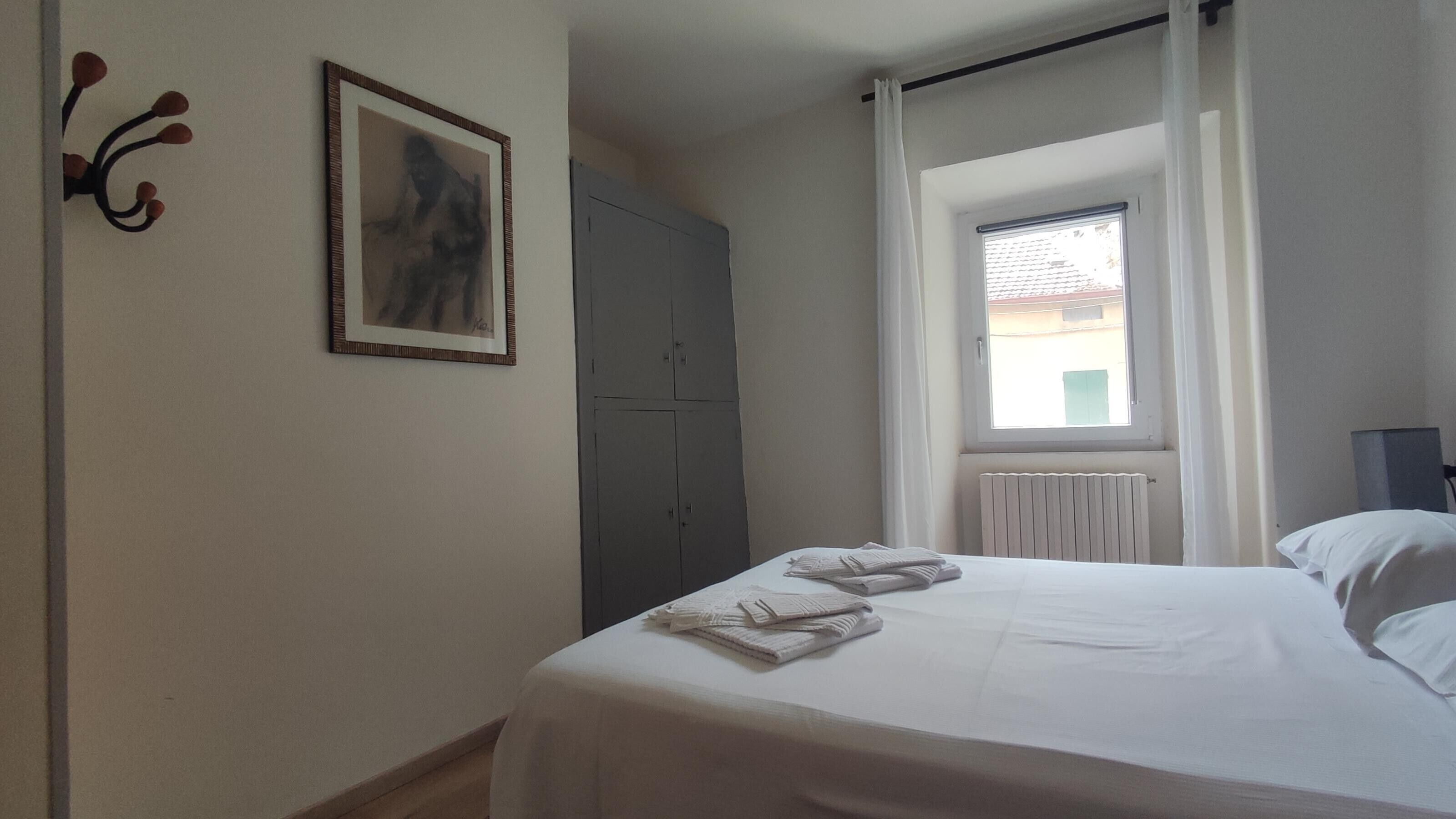 A bedroom with a bed, a window with curtains, a radiator, and a wardrobe.