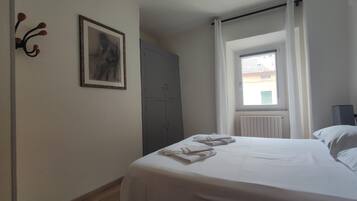 A bedroom with a bed, a window with curtains, a radiator, and a wardrobe.