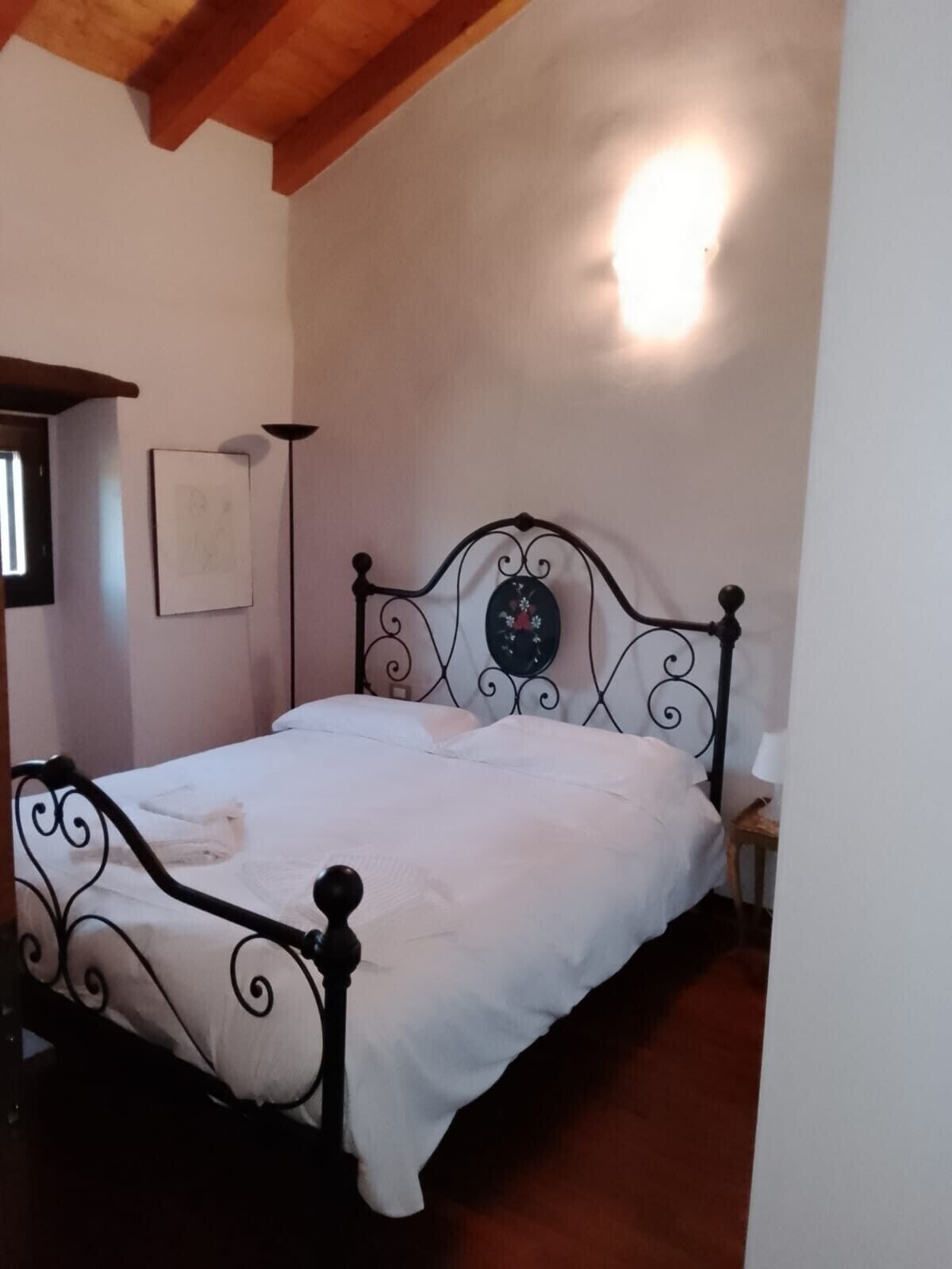 Ein Einzelbett mit Metallgestell, ein Nachttisch, eine Wandlampe und ein gerahmtes Bild an der Wand.