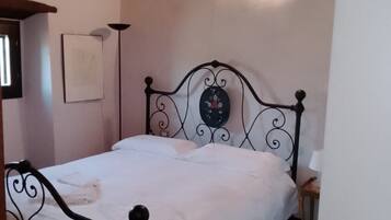 Ein Einzelbett mit Metallgestell, ein Nachttisch, eine Wandlampe und ein gerahmtes Bild an der Wand.