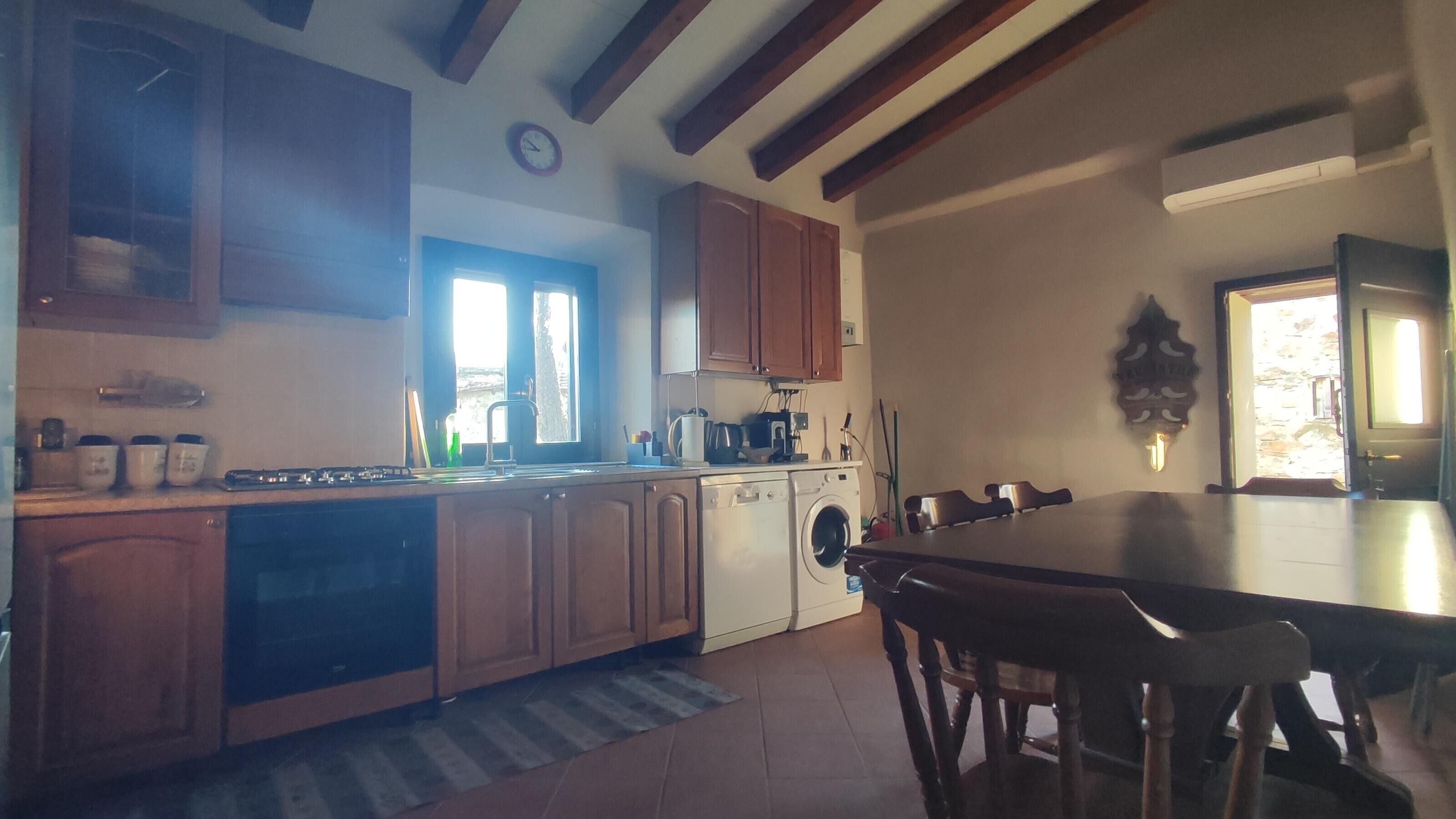 Une cuisine avec des meubles en bois, un lave-linge, une table à manger et une horloge au mur.