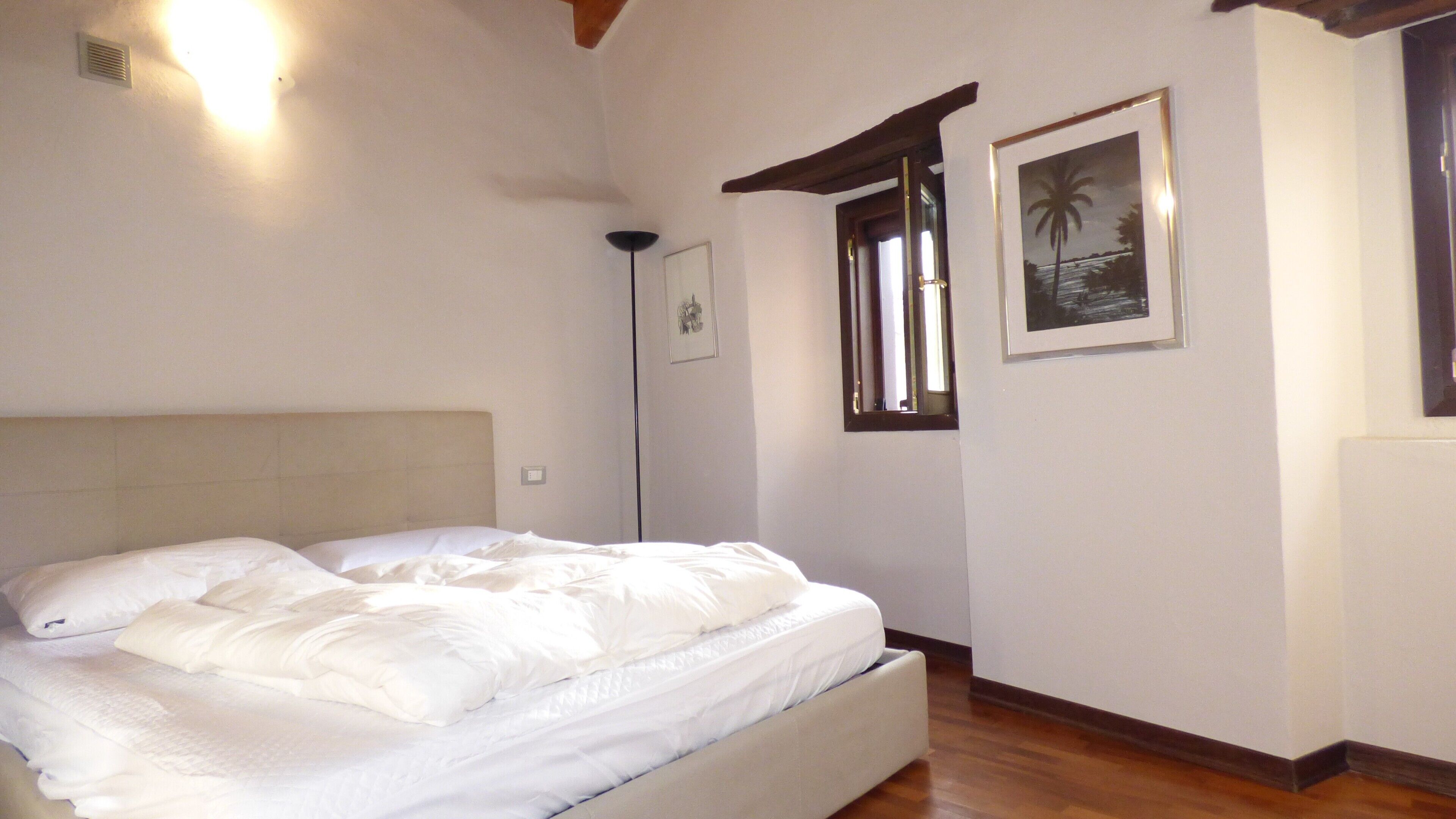Un dormitorio con cama, rejilla en el techo, luz empotrada en la pared, cuadro enmarcado y ventana con vistas.