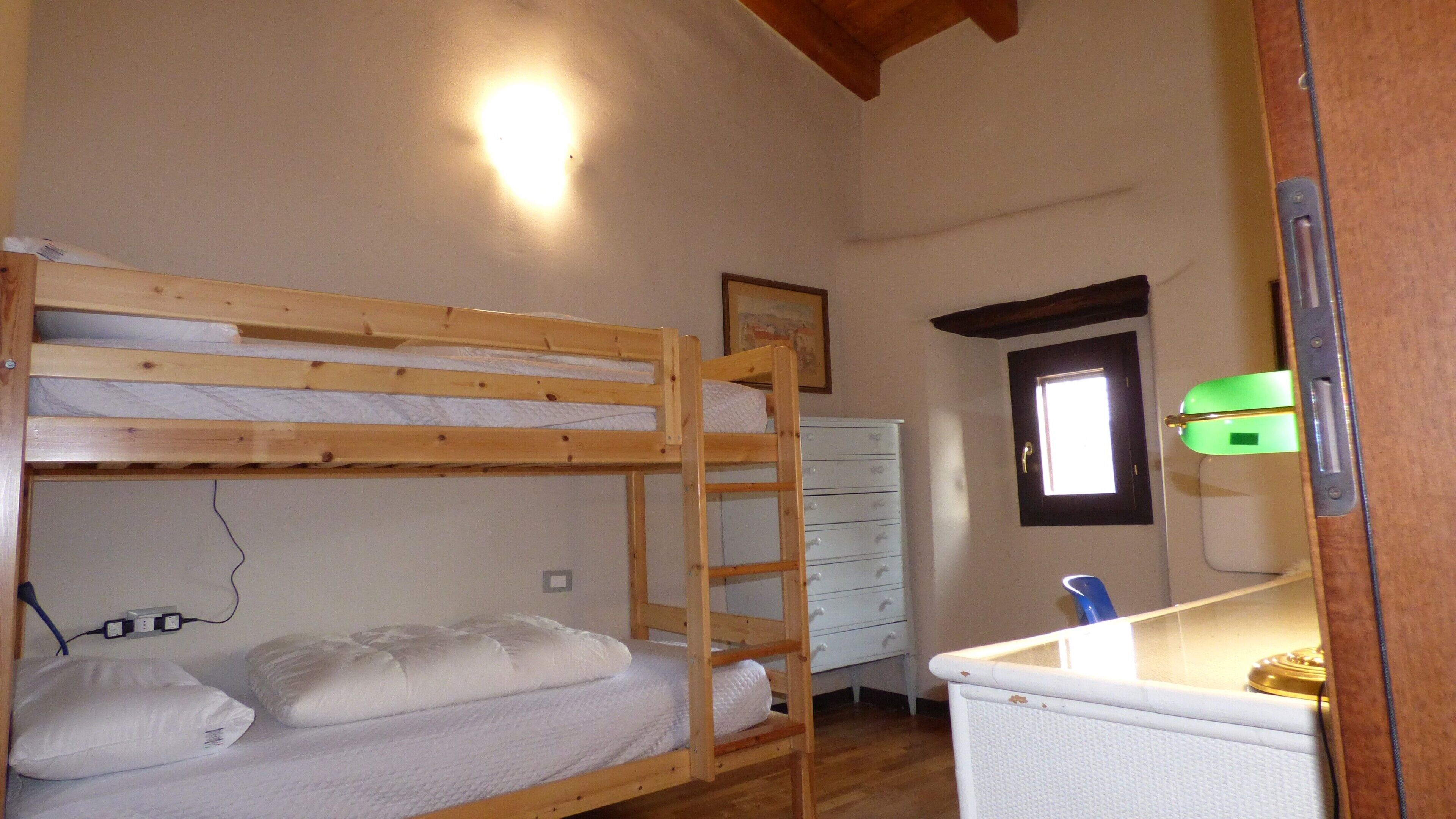 A bunk bed with a ladder, a white dresser, a small window, and a wall socket.